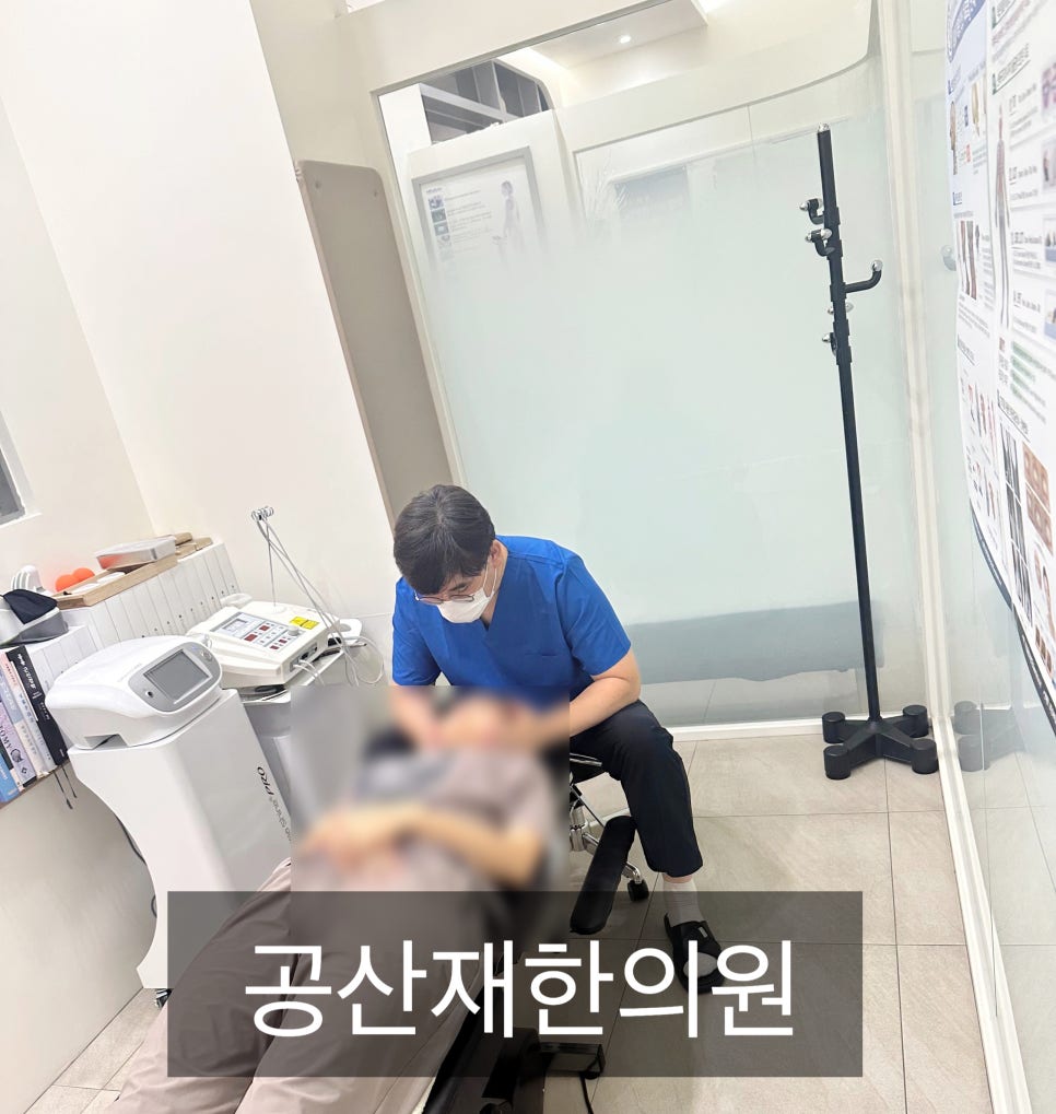 한의원에서 의료진이 환자를 진료하는 모습. 의료 장비가 옆에 놓여 있으며, 벽에는 다양한 정보가 적힌 포스터가 붙어 있다.